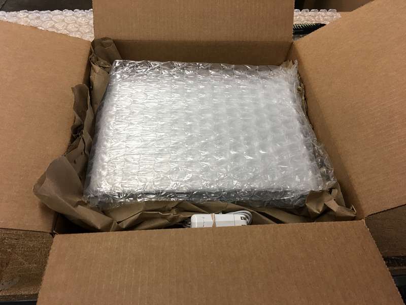 The cheap used Macbook Pro is placed in the shipping box on top of crumpled kraft paper.